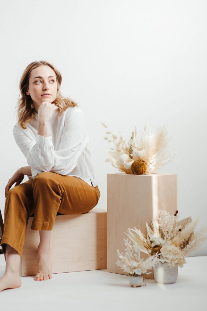 A woman sits beside a dried floral arrangement in a Philadelphia photography studio.