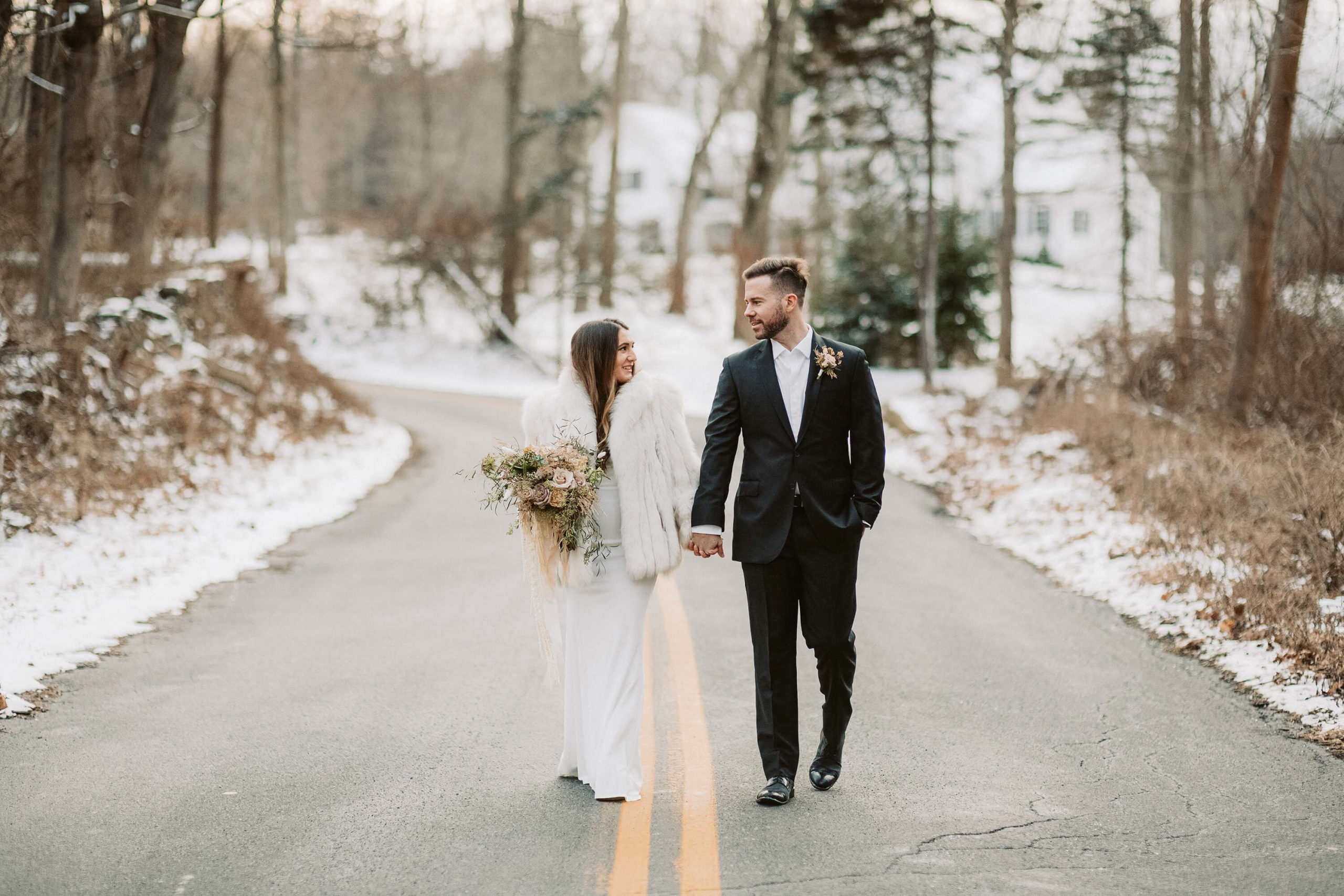 A bride and groom hold hands and walk down a road towards a Philly wedding photographer.