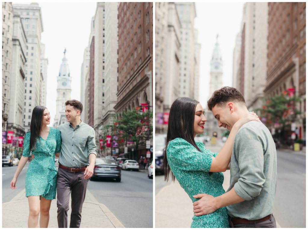 The couple walks down the sidewalk with City Hall in the background during engagement photos in Philadelphia