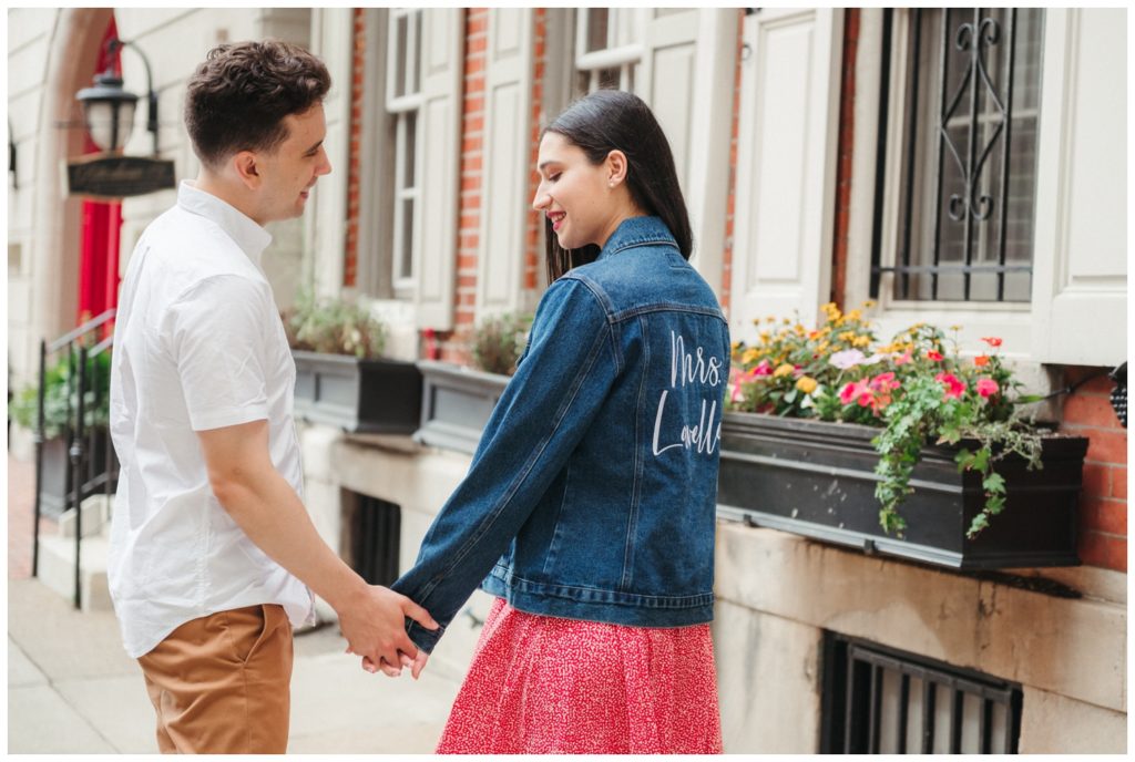 engagement photos in Philadelphia A man and woman hold hands walking past a brick building with a window box