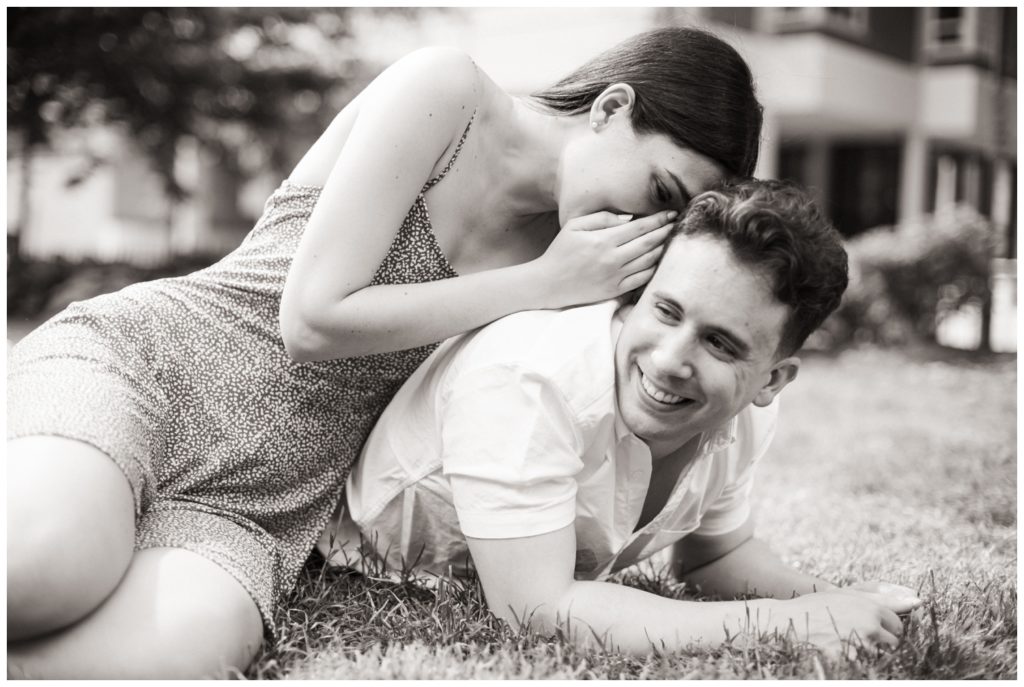 A woman whispers in a man's ear. He laughs. engagement photos in Philadelphia