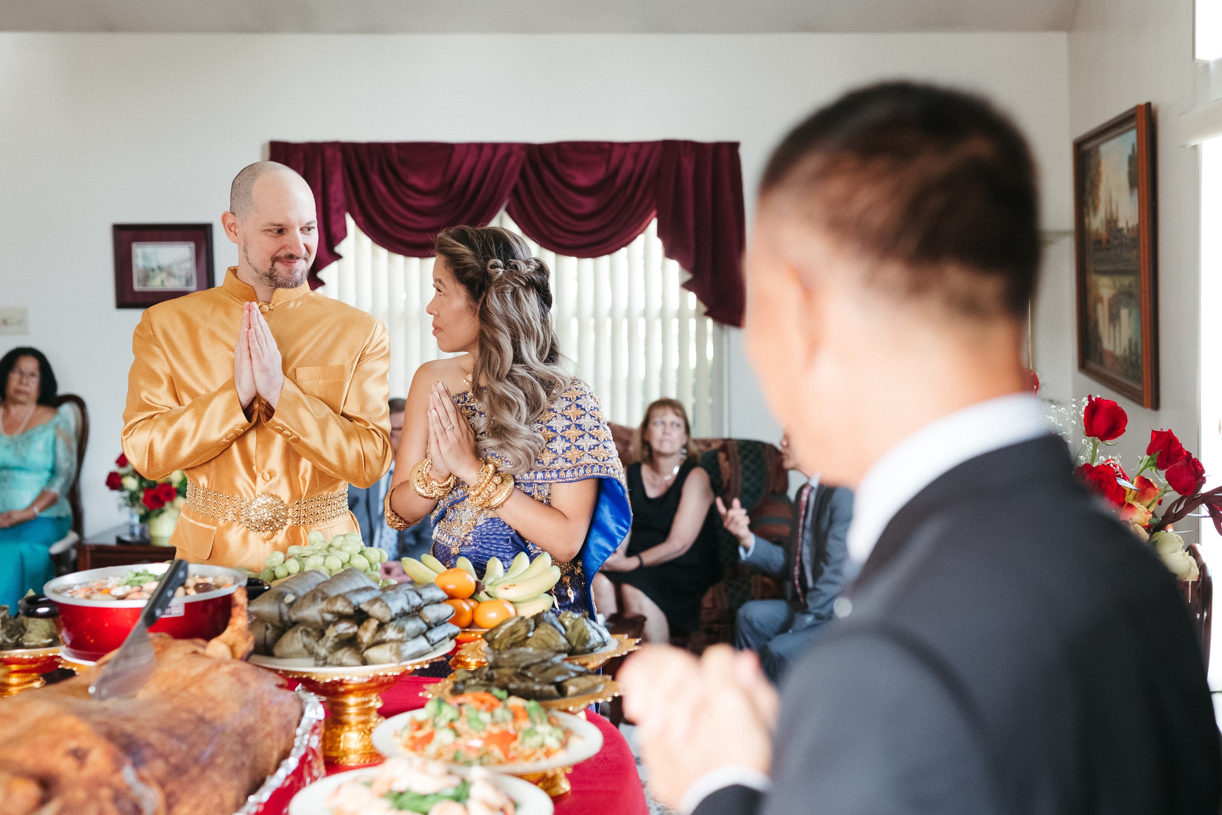 A couple stands by a table of traditional Cambodian food during a Cambodian microwedding in Philly