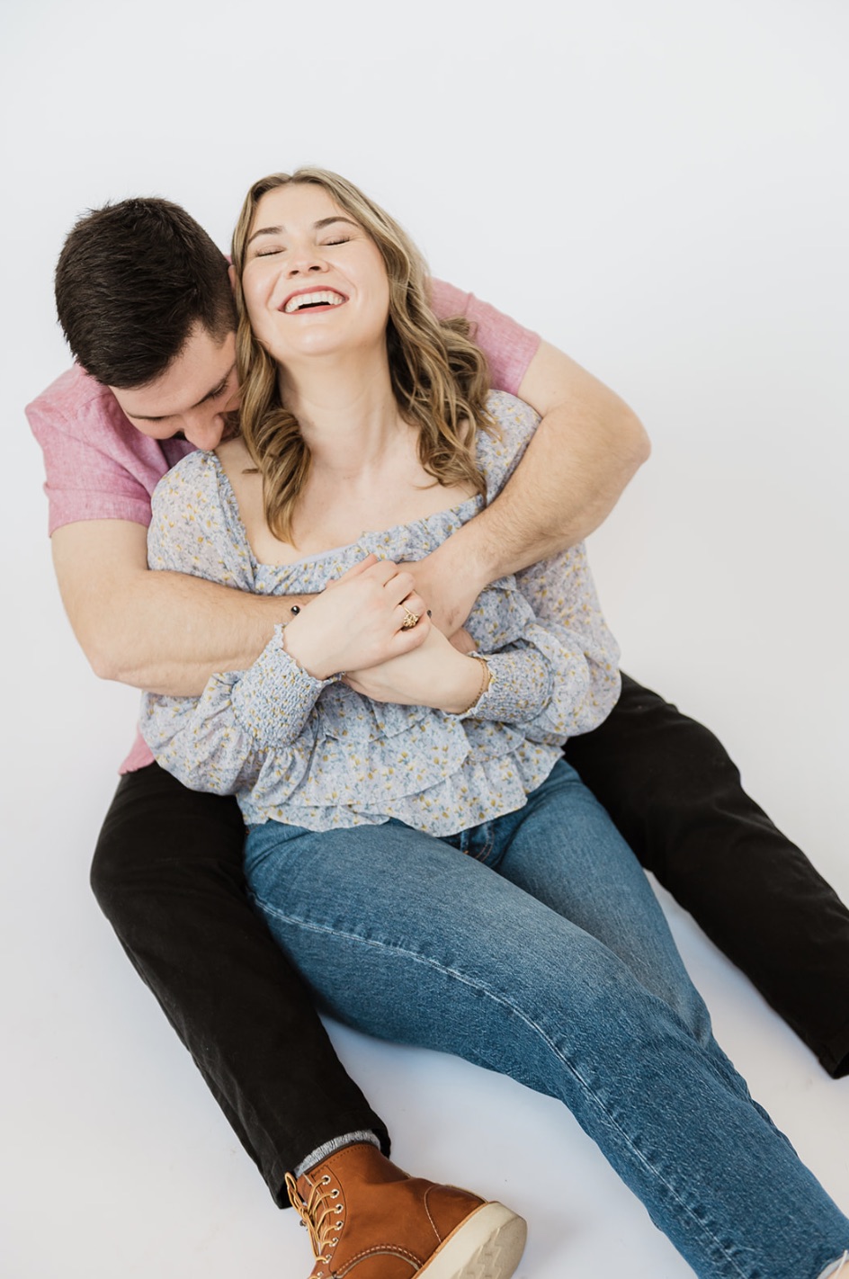 Engagement Session Posing Guide + Outfit Ideas: Couple share an embrace as they both laugh and sit on the floor, taken by Jason Moody