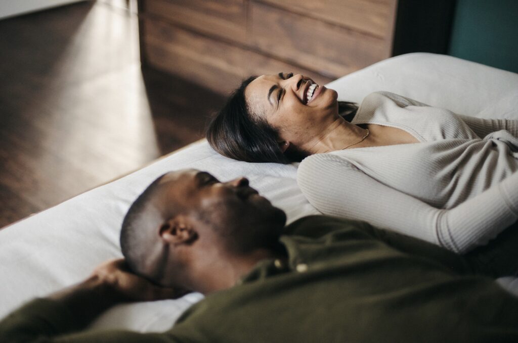 Couple laughing as they lie down together on the bed, captured by Jason Moody Photography