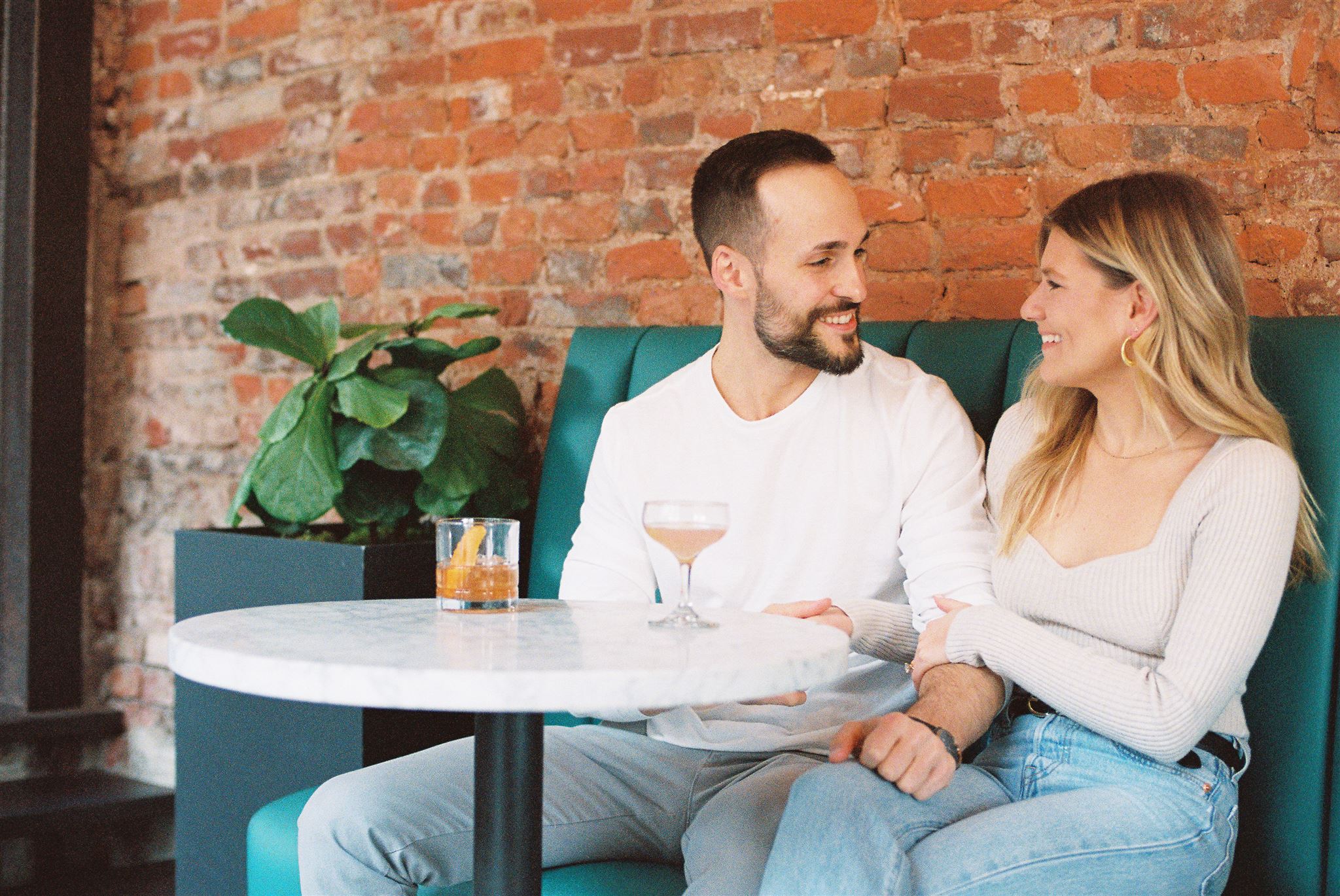 Couple sitting at a table with drinks and smiling at each other during their on-location engagement session