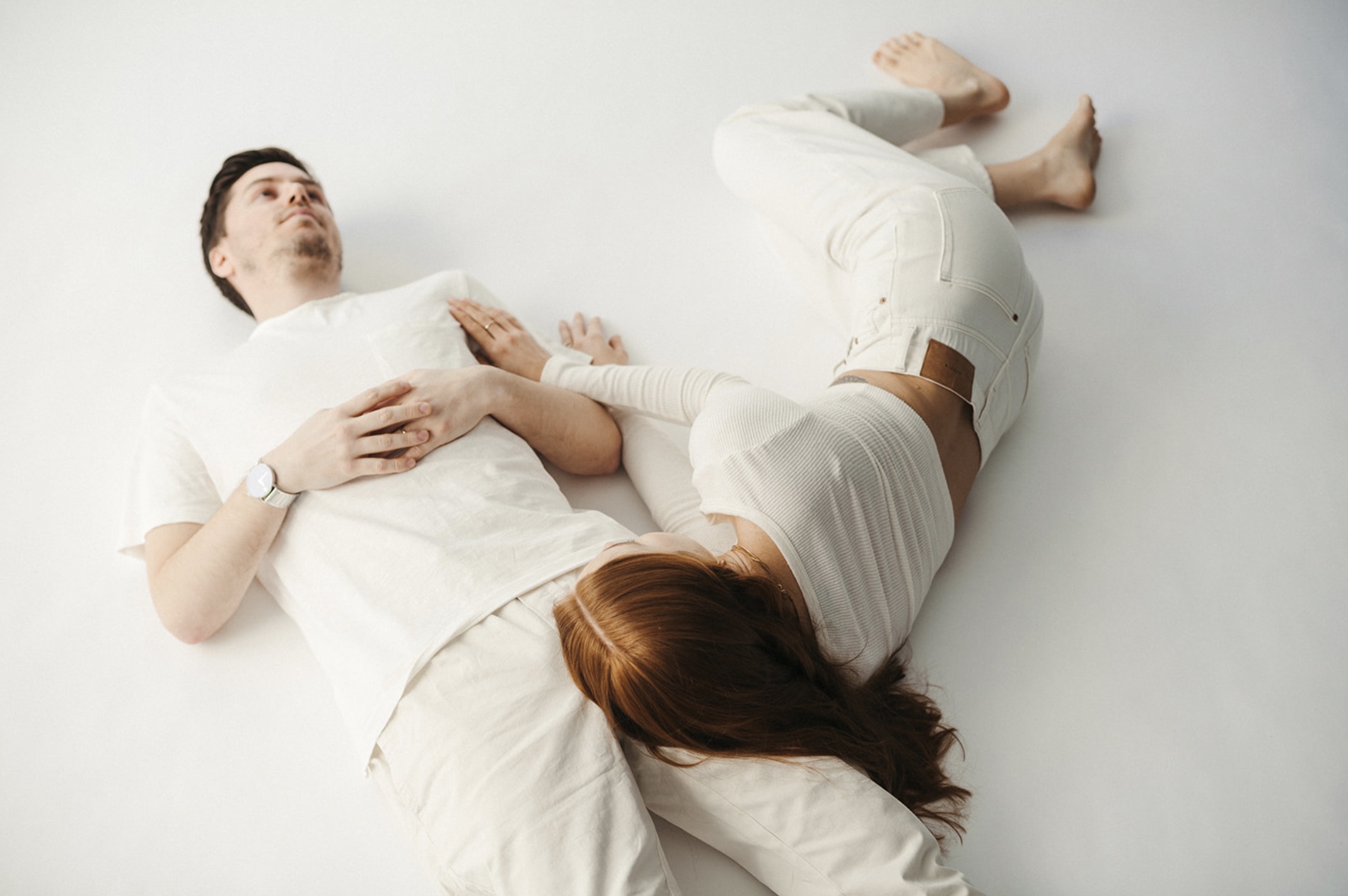 Couple in all white lying down on the white floor of the studio during their engagement session with Jason Moody
