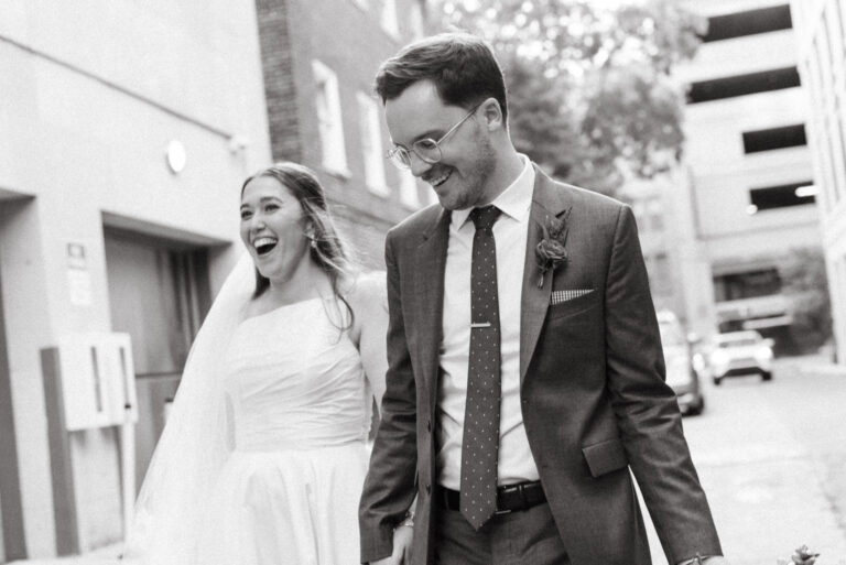 Whimsical Morris House Hotel Wedding: Black and white photo of the bride and groom sharing laughs while they walk, taken by Jason Moody