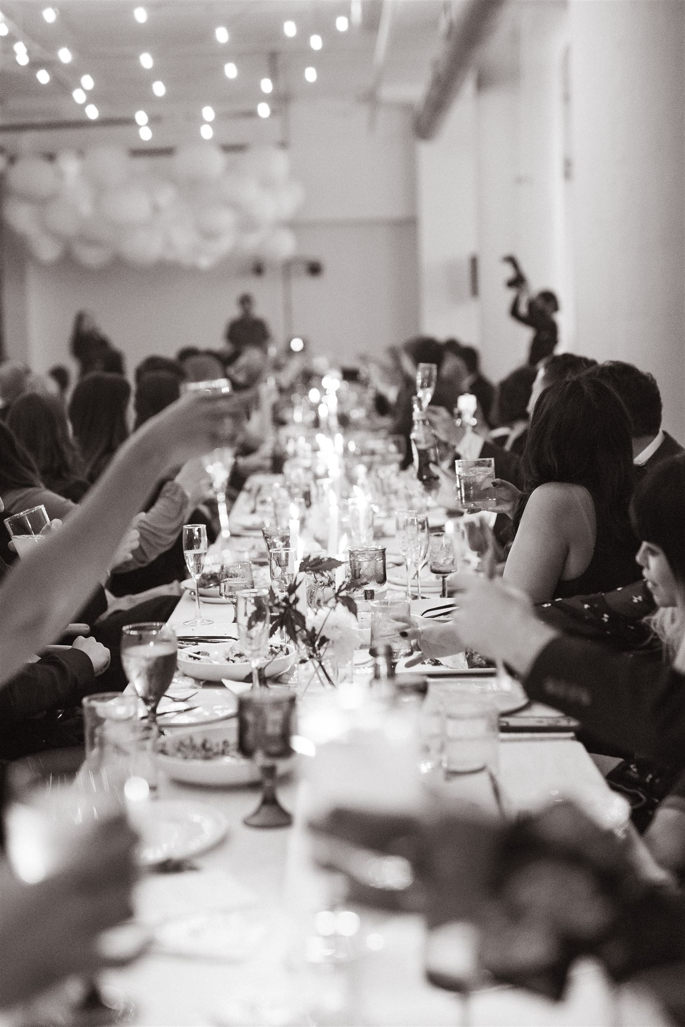 Shot for Kelly Giarrocco - Why is Wedding Photography so Expensive. Black and white photo of the wedding guests raising their glasses during the toast at the wedding reception.