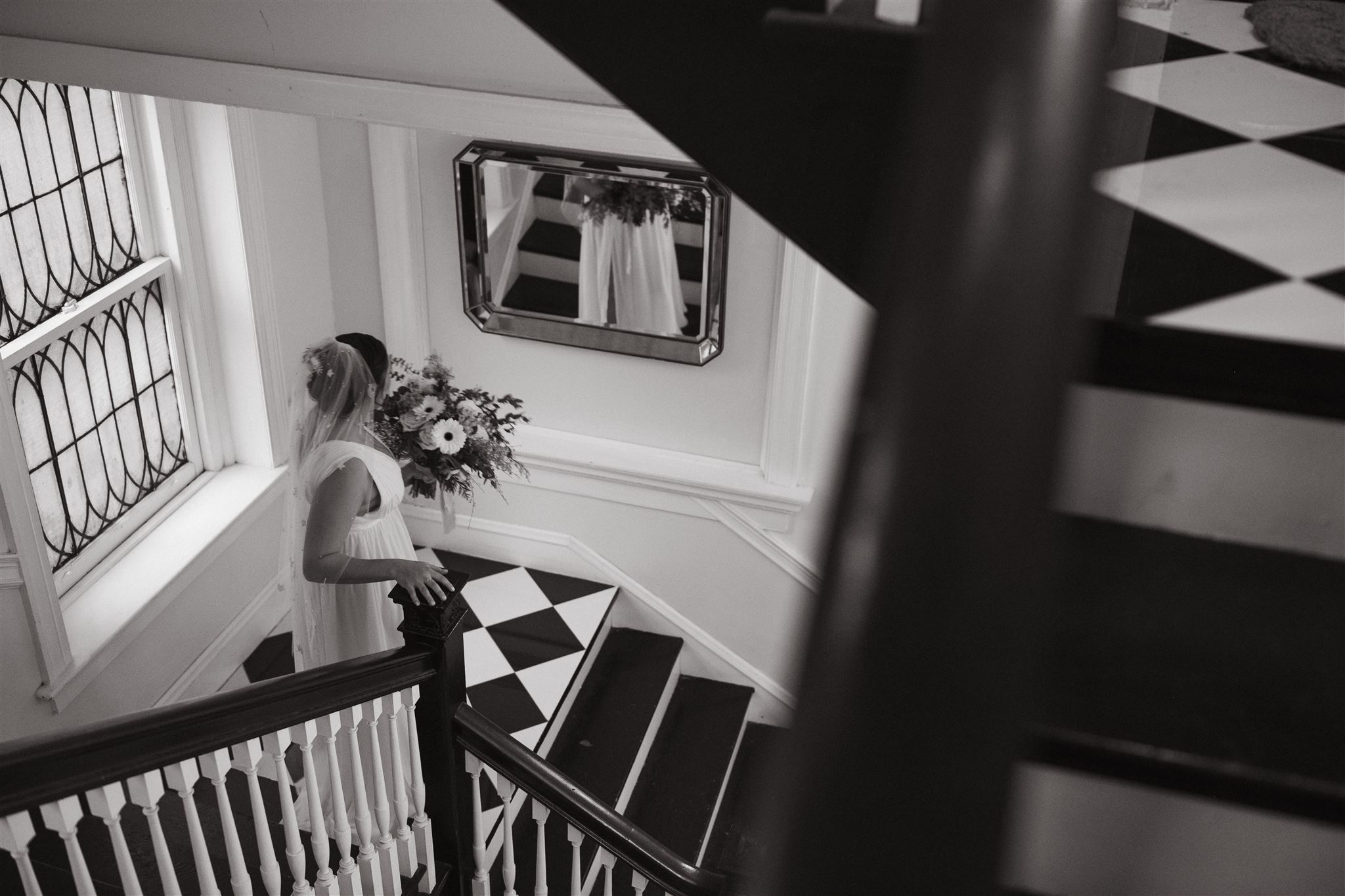 Shot for Jess Flynn - Why is Wedding Photography so Expensive. Black and white photo of bride going down the stairs and looks at her reflection in the mirror.