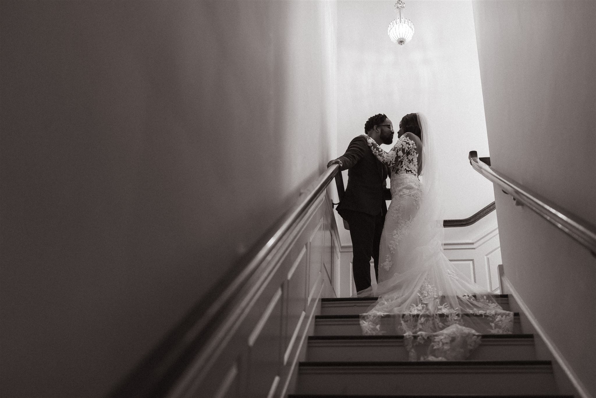 Why is Wedding Photography so Expensive: Black and white photo of couple embracing in the hallway at the top of the stairs.
