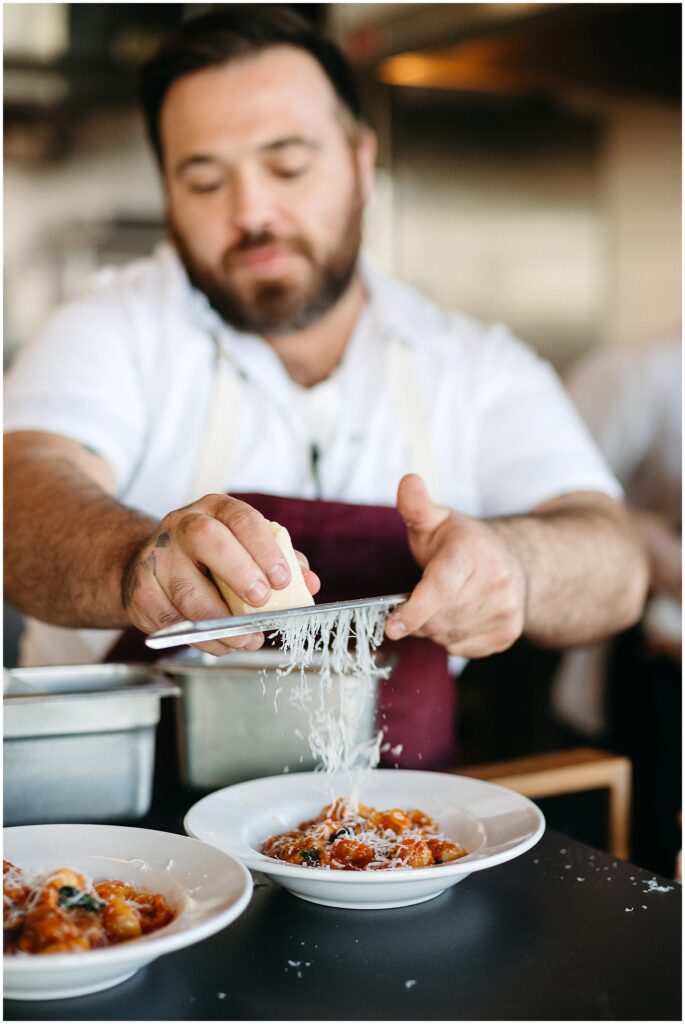 A chef grates cheese over a pasta dish.