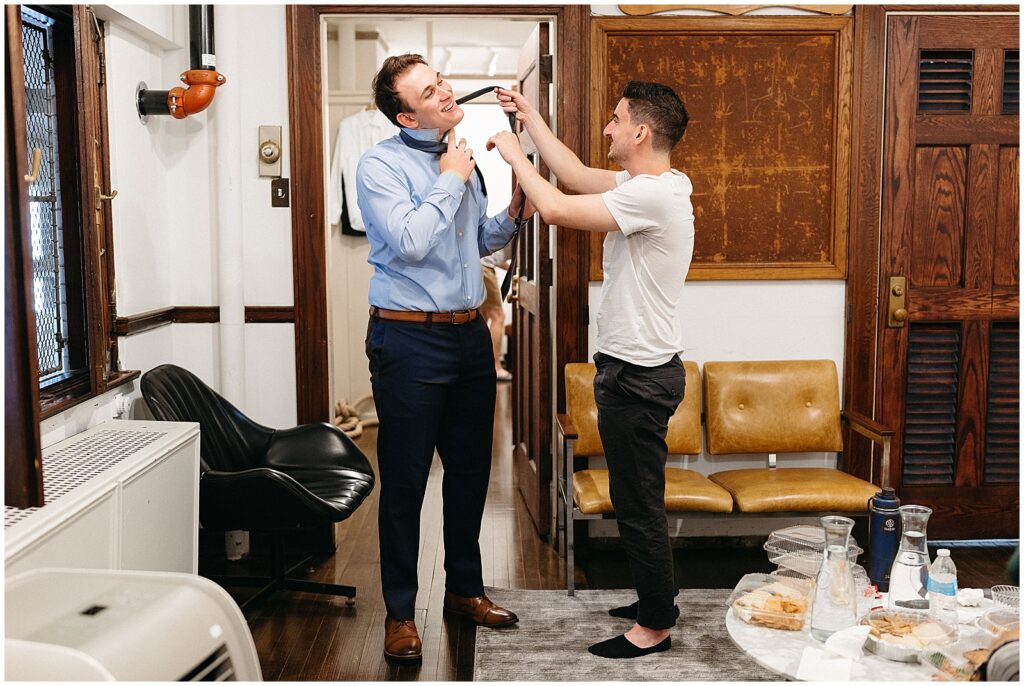 Two groomsmen try to tie a tie in the getting ready suite.