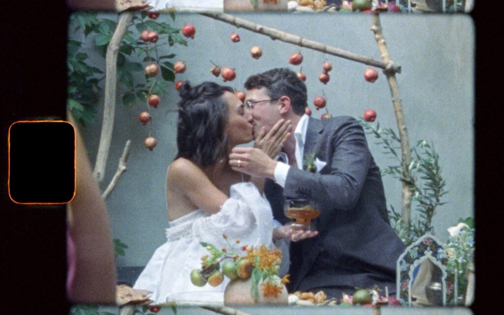 A still from a Super 8 wedding film shows a groom leaning over to kiss a bride.