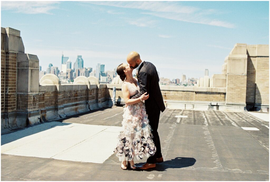 A couple kisses on the rooftop of a Philadelphia wedding venue with the skyline behind them.