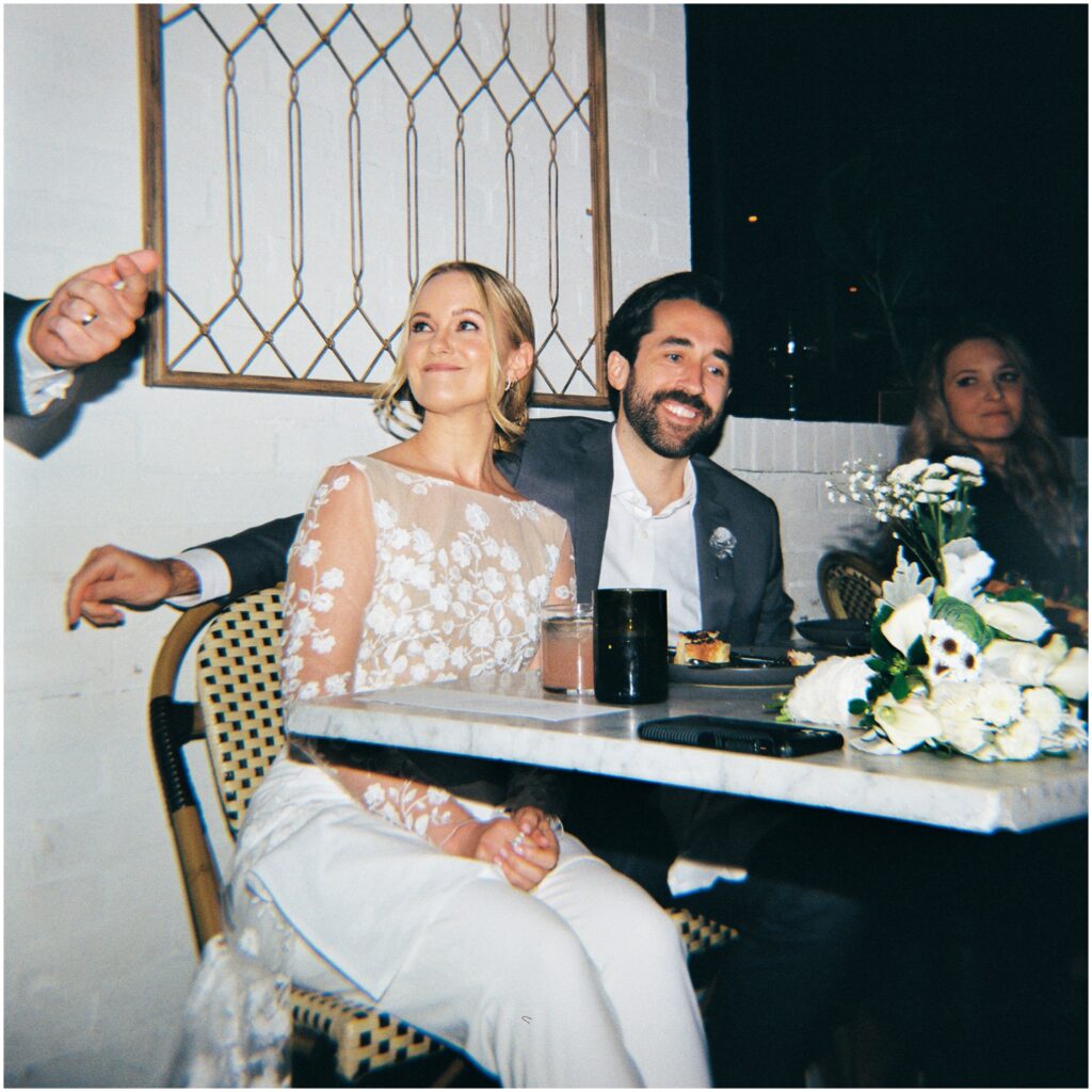 A bride and groom listen to speeches at a rehearsal dinner.