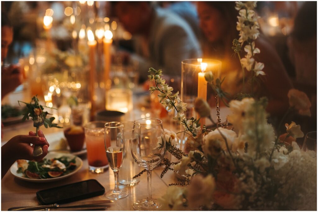 A wedding guest lifts a forkful of salad at a candlelit table.