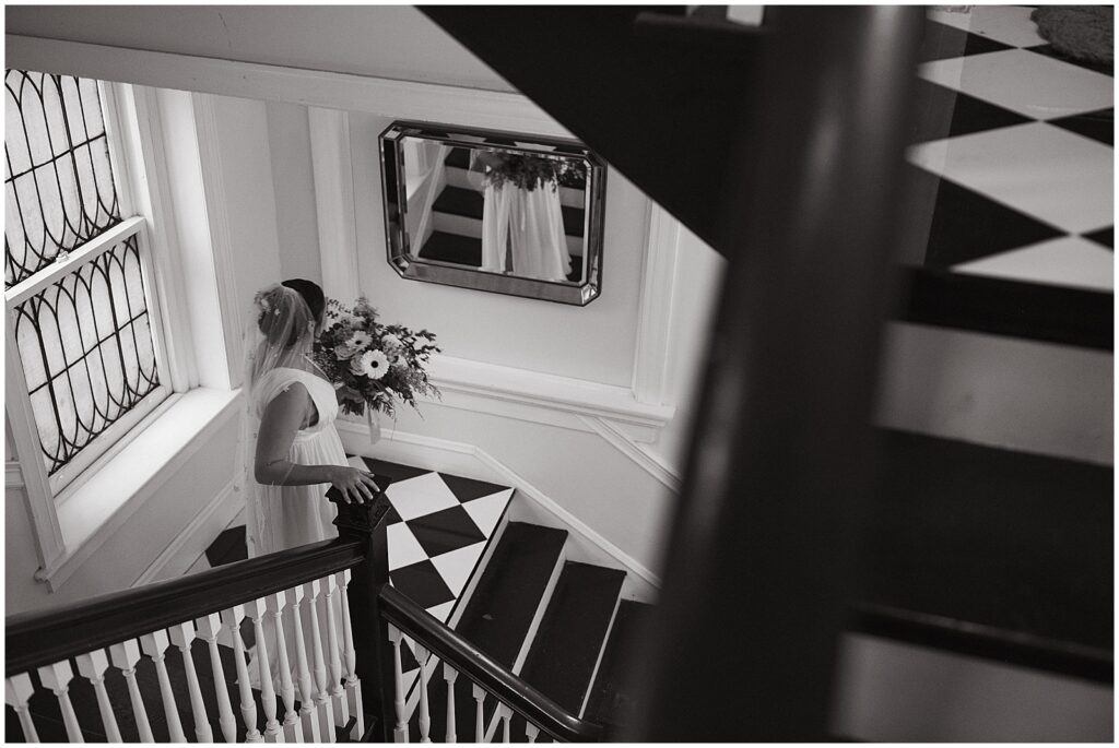 A bride looks in a mirror on her way down a black and white staircase.