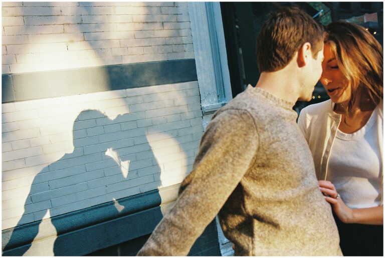 Matt and Jess lean against a low fence casting a shadow in their New York City engagement photos.