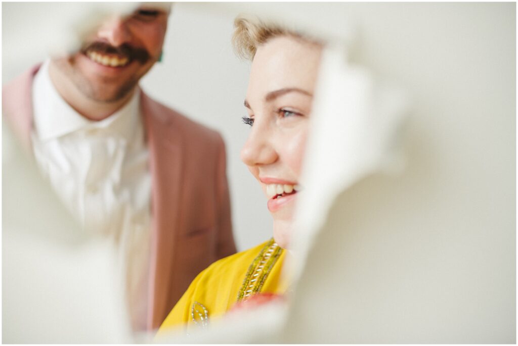 A couple laughs behind a torn studio backdrop posing for wedding photography.