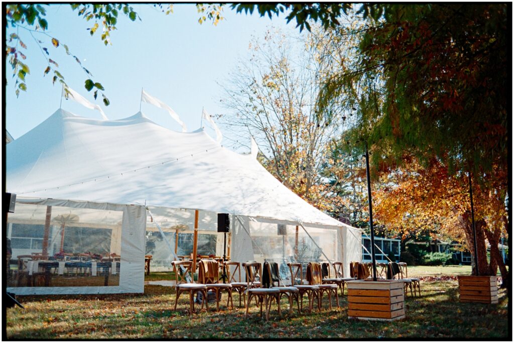 A white tent sits in a yard surrounded by benches for a backyard wedding.