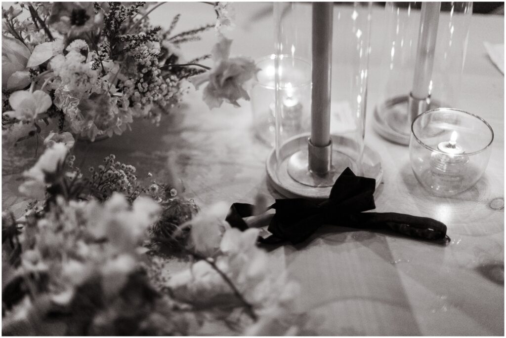 A bowtie sits beside a floral arrangement during a wedding reception.
