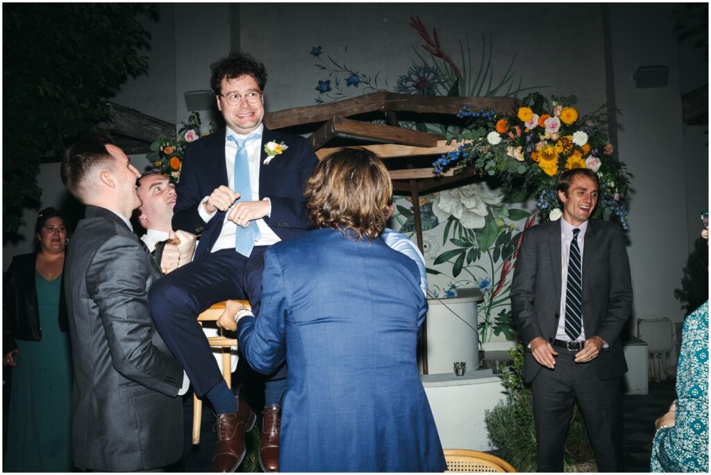Wedding guests lift Owen in a chair for the horah.