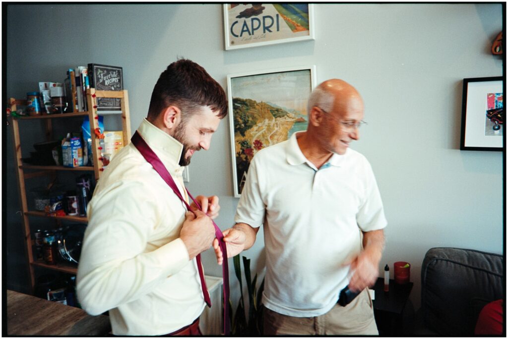 A groom's father pats his arm as he puts on his tie.