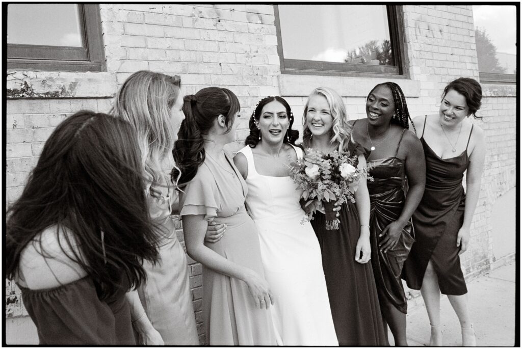 A bride and bridesmaids pose for bridal party portraits against a brick wall.