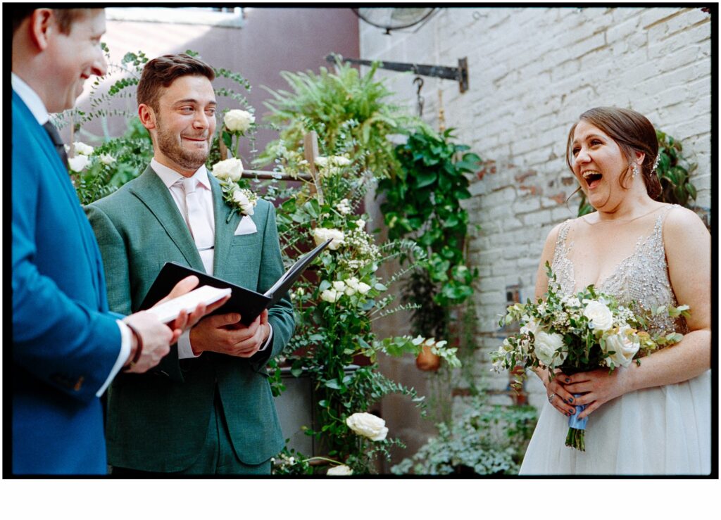 A bride laughs while a wedding officiant makes a funny face.