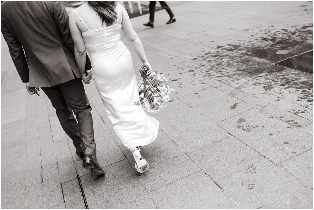 A couple carries a bridal bouquet down a Philadelphia sidewalk on their way to a City Hall elopement.