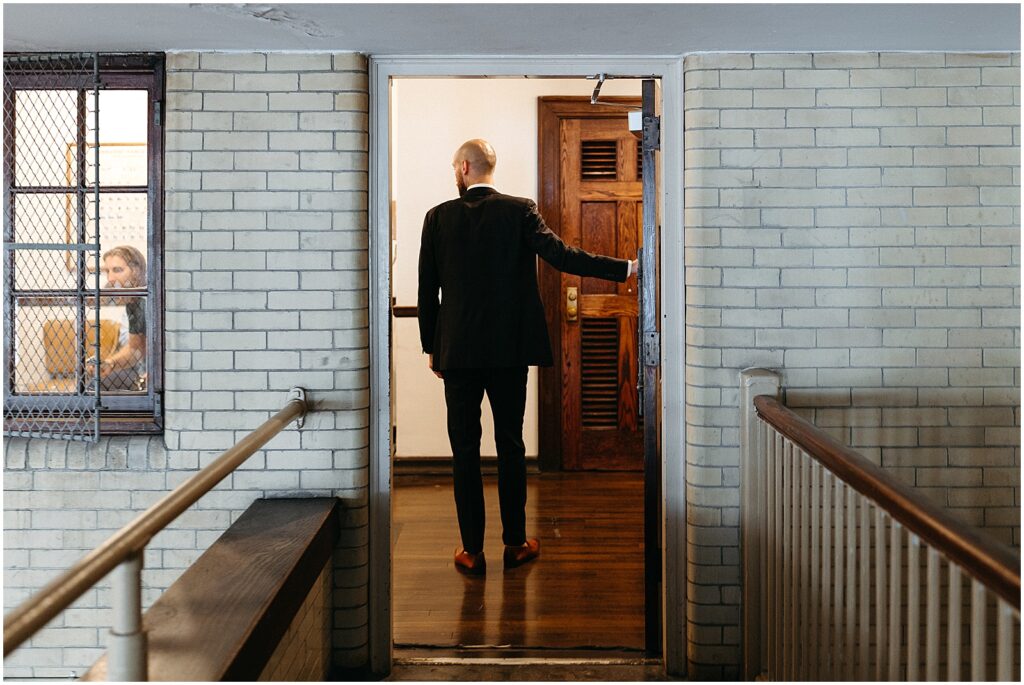 A groom walks through the door of a getting ready suite in an old coach's office.