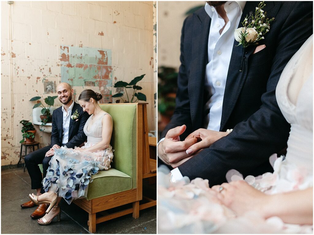 A bride and groom sit on a vintage sofa holding hands.