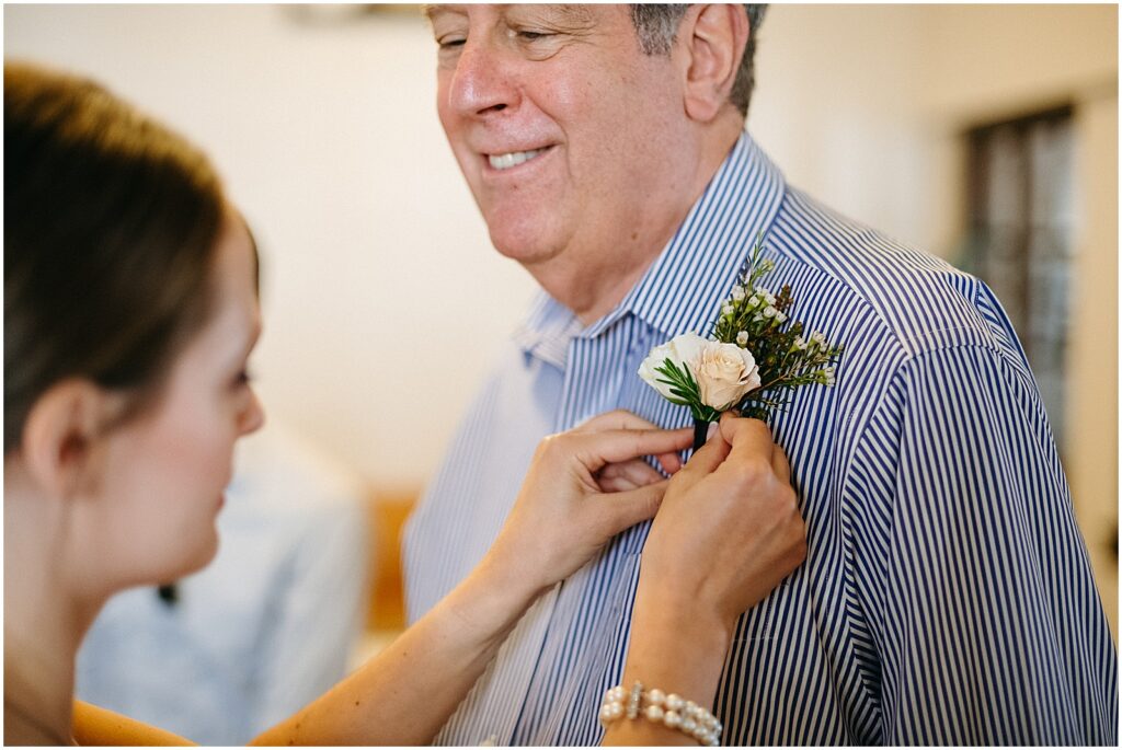 A bride pins a flower to her father's shirt.