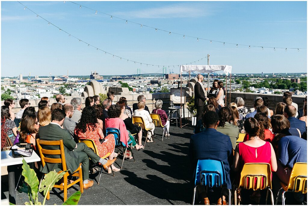 Wedding guests sit in colorful chairs for a rooftop wedding in Philadelphia.