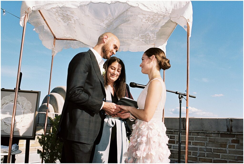 A bride and groom hold hands under a chuppah at a rooftop wedding at the BOK Building.
