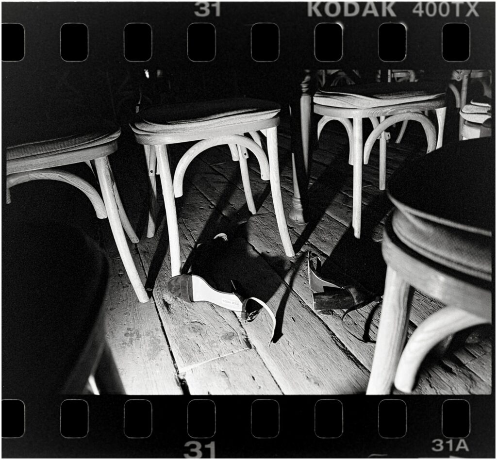 A light illuminates a high heel laying under a chair in a black and white film wedding photo.