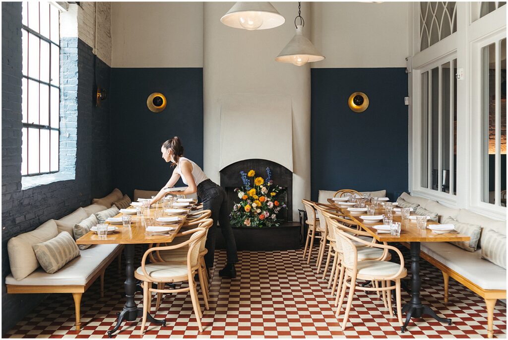 A server sets plates on two long tables for a restaurant wedding in a private dining room in Philadelphia.