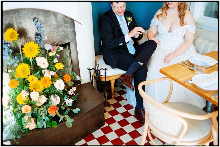 A bride and groom sit in the corner of Suraya beside a colorful floral arrangement at their restaurant wedding.