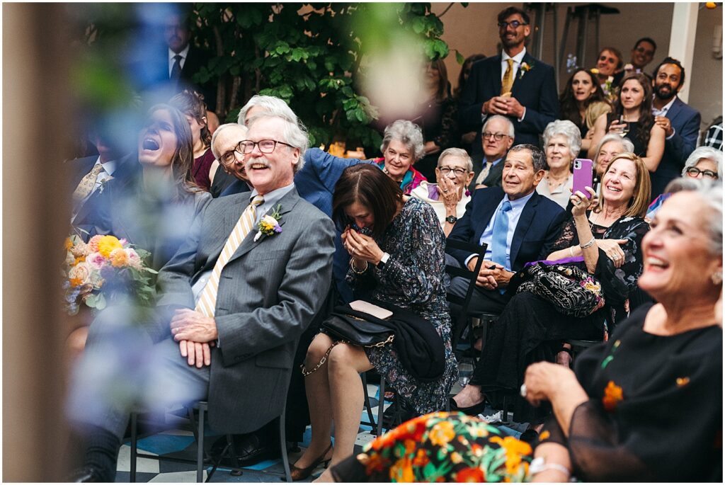 Wedding guests laugh and wipe away tears in a restaurant courtyard.