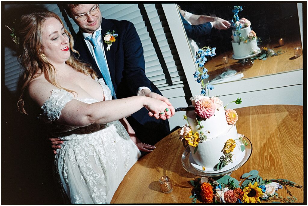 A bride and groom cut into a wedding cake decorated with vibrant flowers.