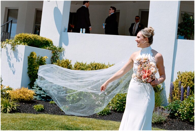 A Philadelphia bride poses on a lawn with her veil blowing in the wind.