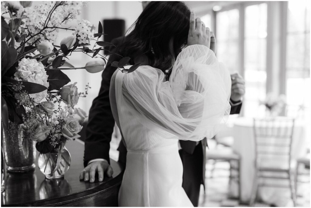 A bride in a wedding dress with puffy sleeves pushes her hair back from her face.