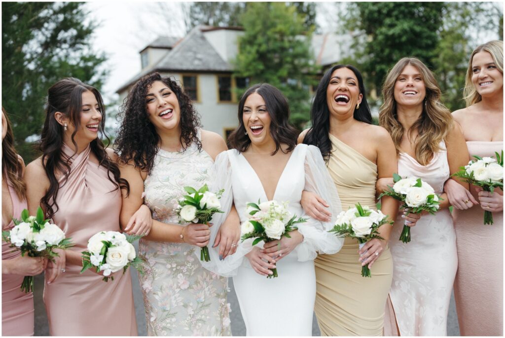 A Philadelphia bride poses with smiling bridesmaids wearing different dresses in neutral colors.