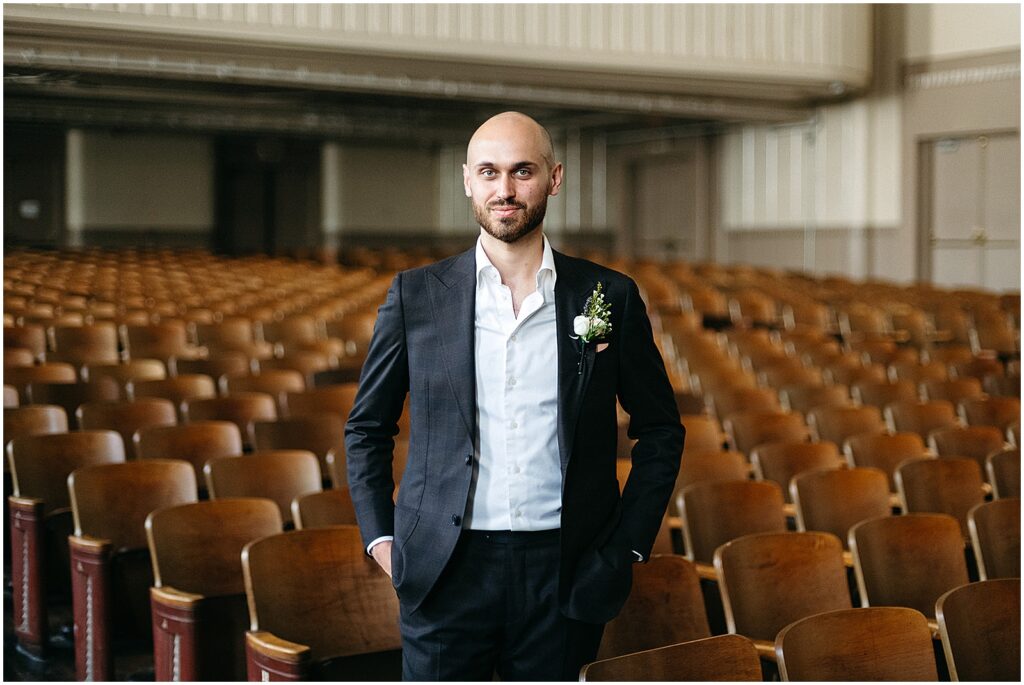 A groom poses at the front of an auditorium and smiles at a Philadelphia wedding photographer.