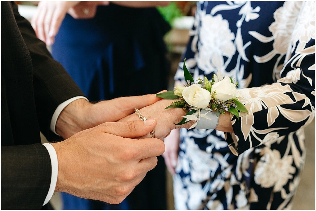 A bride holds his mother's hand and looks at the corsage he gave her.