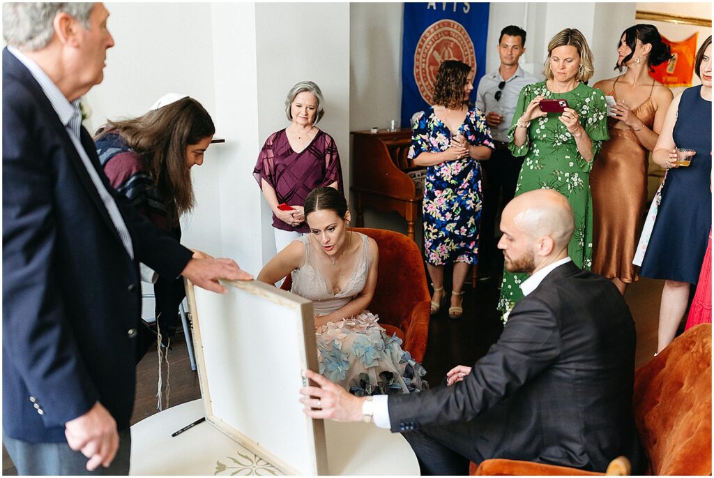 A Philadelphia bride and groom sit and read their ketubah while family members watch.