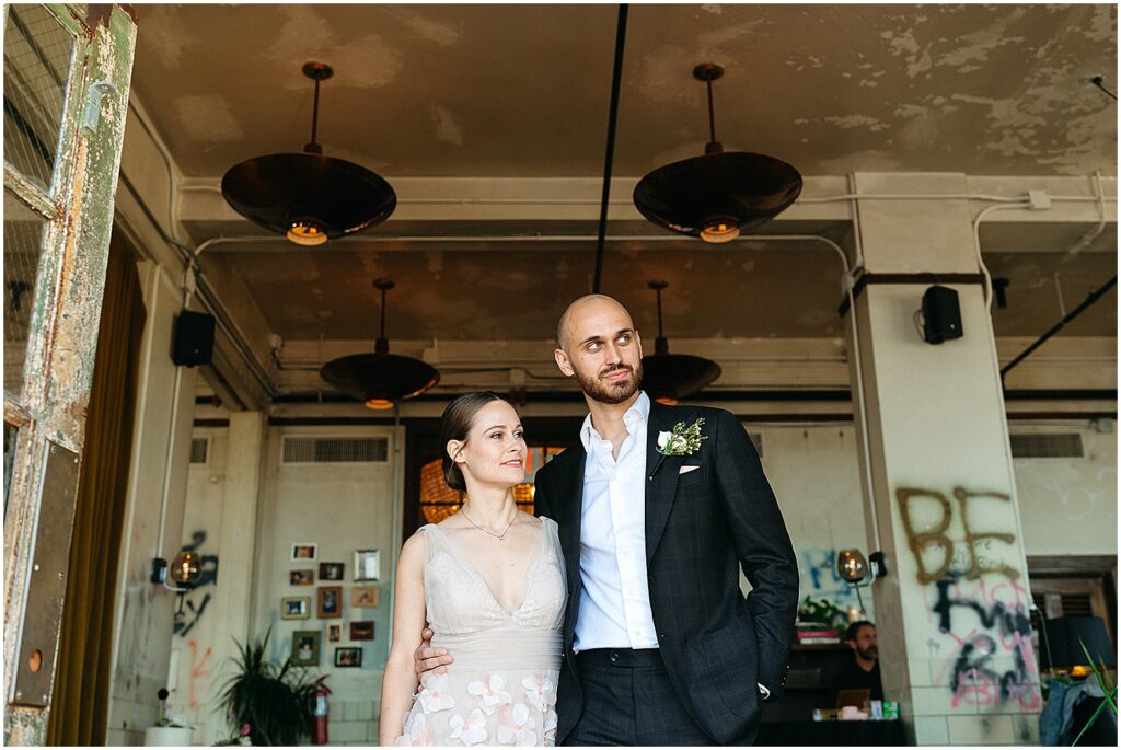 A bride and groom stand in the doorway of Irwin's overlooking the rooftop wedding venue.