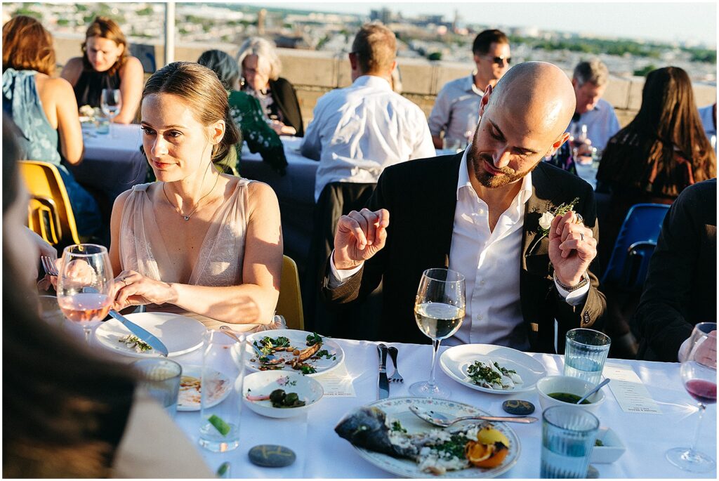 A bride and groom eat dinner with guests at Irwin's rooftop.