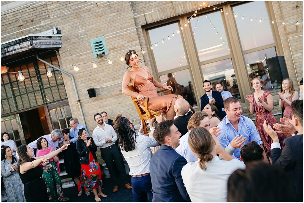 Guests raise a family member on a chair under strings of lights on Irwin's rooftop.