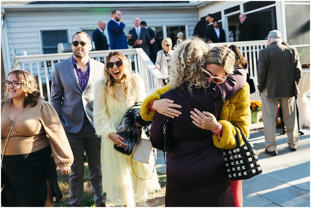 Wedding guests embrace as they arrive at a lake house for a wedding.